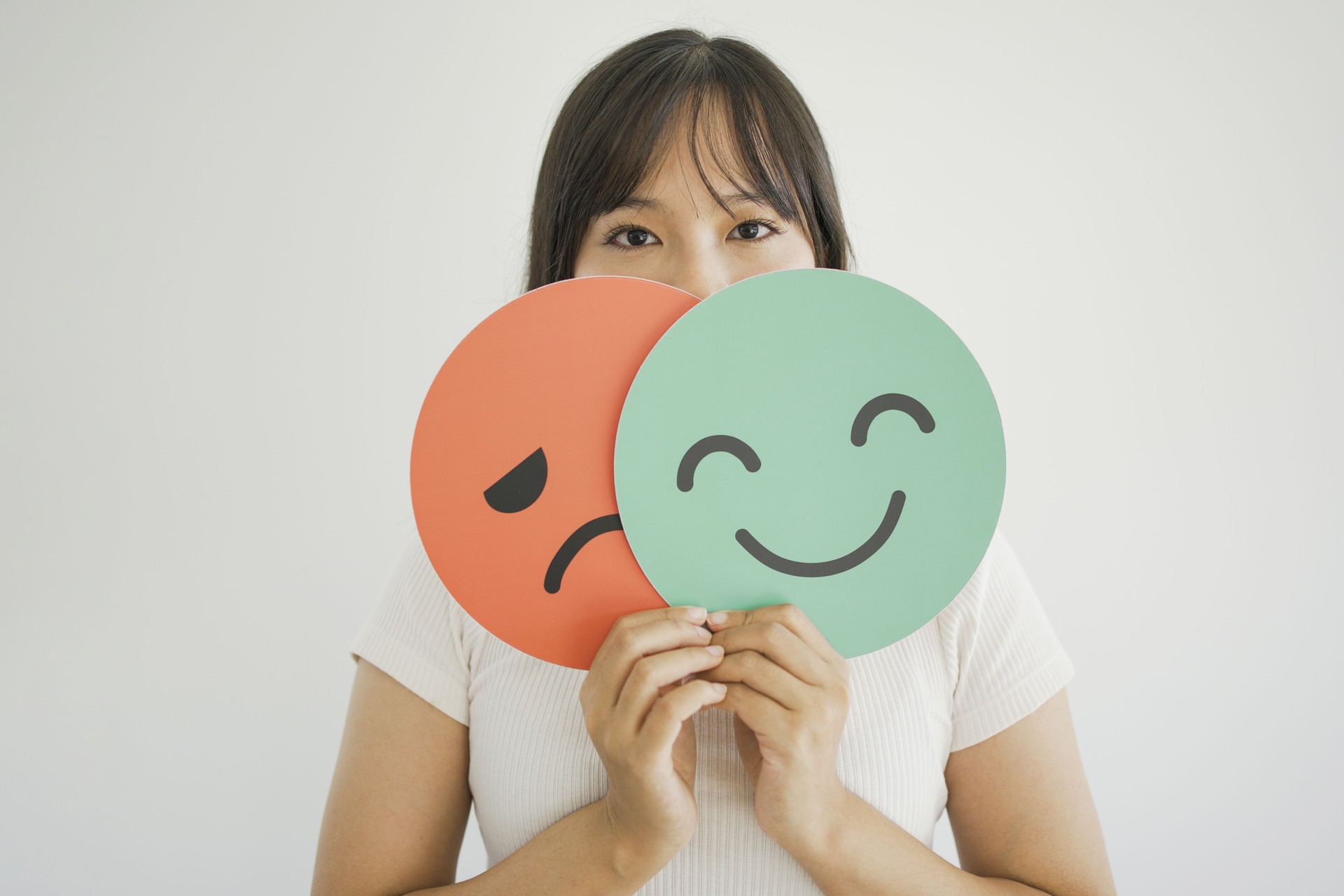 Woman hands holding sad face hiding behind happy face, bipolar and depression, mental health, split personality, mood change concept